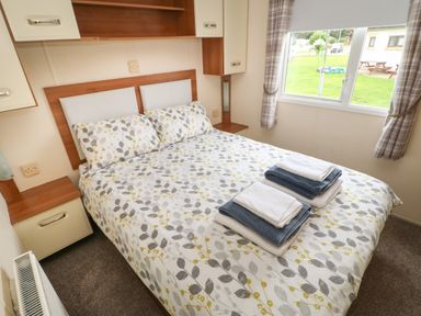 A bedroom with a double bed with patterned bedding towels on the bed a window with curtains and bedside cabinets at Hedgehog Retreat in Felton