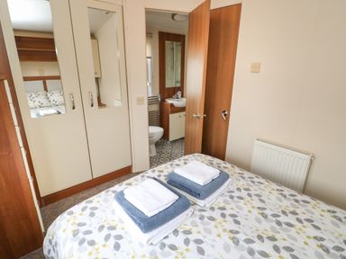 A bedroom with a bed with folded towels on it a wardrobe with mirrors and a door leading to a bathroom at Hedgehog Retreat in Felton