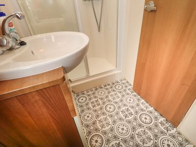 A bathroom with a sink wooden cabinet patterned tile floor shower and wooden door at Hedgehog Retreat in Felton