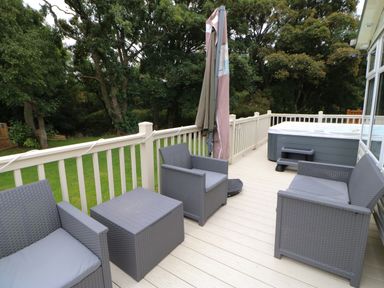 An outdoor deck with gray wicker chairs and a table a closed umbrella and a hot tub at Hedgehog Retreat in Felton