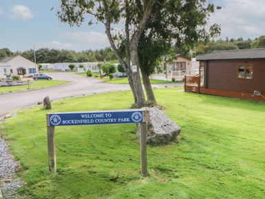 A park entrance with a welcome sign and trees by a road with houses at Bockenfield Country Park in Felton