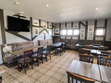 A dining area with tables chairs and bench seating a wall mounted television and framed pictures at Hedgehog Retreat in Felton
