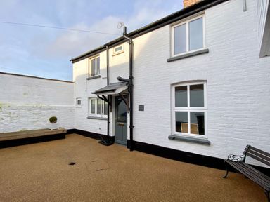An exterior courtyard with a white brick house entrance bench and a small planter at Secret Cottage Southwold