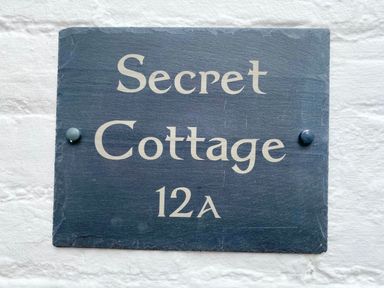 A black house sign reading Secret Cottage 12A mounted on a white wall at Secret Cottage Southwold