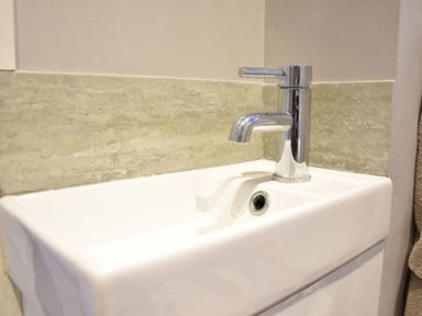 A bathroom sink with a chrome faucet and grey tiled backsplash at Secret Cottage Southwold