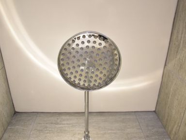 A close-up of a chrome showerhead against a tiled wall at Secret Cottage Southwold