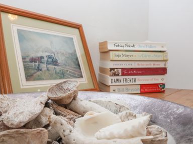 A bowl with dried shells and wood pieces with a stack of books and a framed painting of a train in the background at Secret Cottage Southwold
