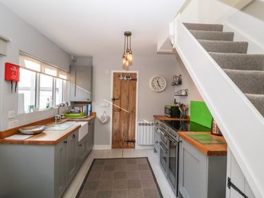 A kitchen with grey cabinets wooden countertops a stove a microwave a sink and stairs at Secret Cottage Southwold