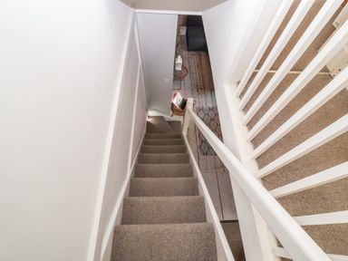 A carpeted staircase with white walls and railing leading down to a hallway with wooden floors and furniture at Secret Cottage Southwold
