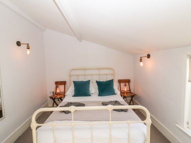 A bedroom with a metal framed bed two teal pillows wooden side tables lamps on tables and wall lights at Secret Cottage Southwold