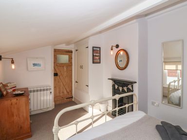 A bedroom with a white metal bed frame wooden door wooden dresser and wall mirror at Secret Cottage Southwold