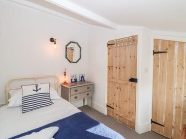 A bedroom with a metal bed frame a side table with a lamp and a mirror wooden doors at Secret Cottage Southwold