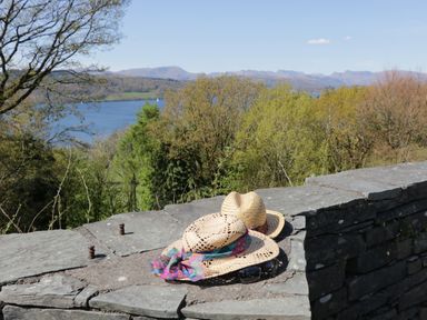 A stone wall with two straw hats and sunglasses with trees lake and mountains in the background at 6 Calgarth View in Windermere