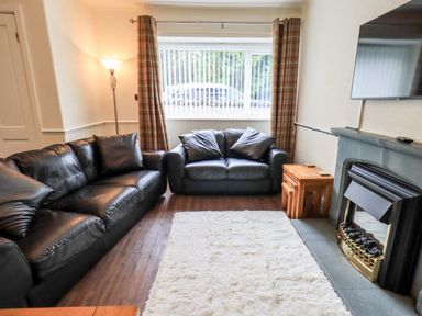 A living room with black leather sofas a white rug wooden nesting tables a floor lamp and a fireplace at 6 Calgarth View in Windermere