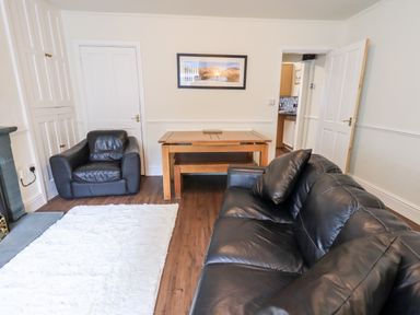 A living room with black leather sofas a wooden dining table and bench a white rug and a fireplace at 6 Calgarth View in Windermere