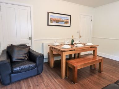 A dining area with a wooden table set with plates glasses and a bottle next to a black armchair at 6 Calgarth View in Windermere