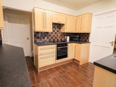 A kitchen with wooden cabinets black countertops tiled floor a built in oven microwave and two white doors at 6 Calgarth View in Windermere