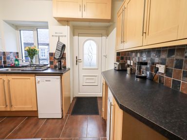 A kitchen with wooden cabinets dishwasher flowers on the counter and a door at 6 Calgarth View in Windermere