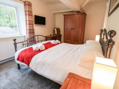 A bedroom with a metal framed bed with white bedding and red runner and towels a wooden wardrobe dressing table and a wall mounted television at 6 Calgarth View in Windermere