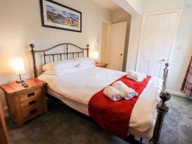 A bedroom with a metal bed frame white bedding red runner and towels on the bed at 6 Calgarth View in Windermere