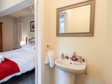 A bedroom with a white bedspread and red throw next to a small sink with a mirror above at 6 Calgarth View in Windermere
