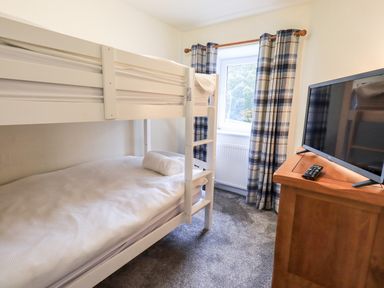 A bedroom with a white bunk bed a wooden cabinet with a television and a window with plaid curtains at 6 Calgarth View in Windermere