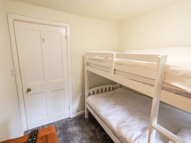 A small bedroom with a white bunk bed a wooden table with remote controls and a closed white door at 6 Calgarth View in Windermere