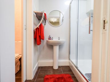 A bathroom with a pedestal sink red towels a round mirror a shower enclosure and a toilet at 6 Calgarth View in Windermere