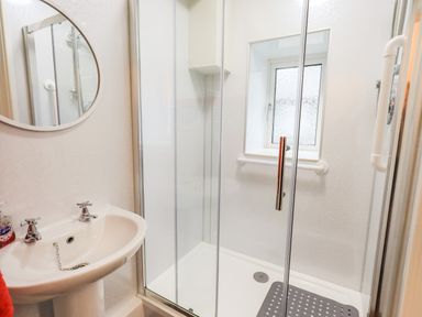 A bathroom with a sink a round mirror and a glass shower enclosure with a window at 6 Calgarth View in Windermere