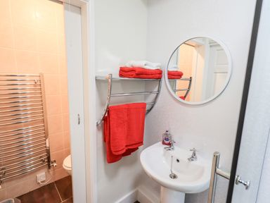 A bathroom sink with a round mirror and red towels on a metal rack at 6 Calgarth View in Windermere