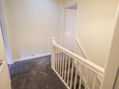 A carpeted hallway with white walls a white banister a radiator and an open door at 6 Calgarth View in Windermere