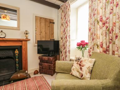 A living room corner with green armchair, floral cushion, TV on stacked storage boxes, wooden fireplace, and floral curtains at 12 Castlegate in Pickering
