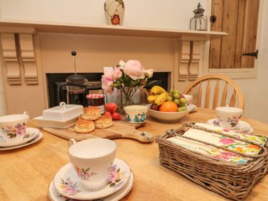 A wooden table set with floral teacups scones jam fresh fruit flowers and napkins at 12 Castlegate in Pickering