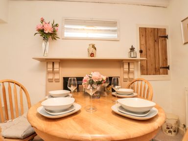 A dining area with a wooden round table set with plates bowls wine glasses and pink flowers at 12 Castlegate in Pickering