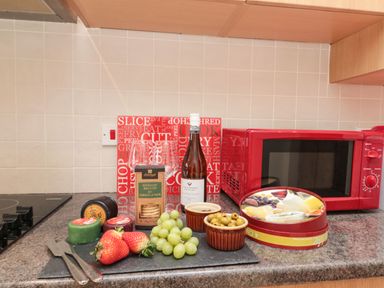 A kitchen countertop with a red microwave cutting boards wine bottle glasses cheese crackers strawberries grapes and olives at 12 Castlegate Pickering