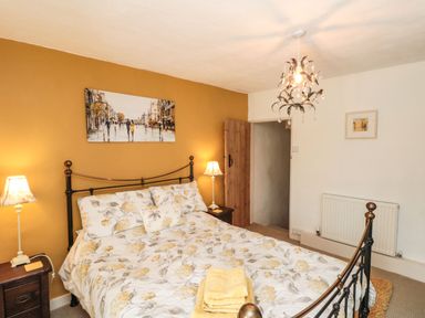 A bedroom with a bed with floral bedding two bedside tables with lamps a painting on a mustard wall and a chandelier at 12 Castlegate in Pickering