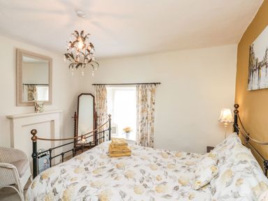 A bedroom with a floral patterned bedspread a chandelier a mirror wicker chair and a window with floral curtains at 12 Castlegate in Pickering