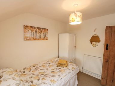 A bedroom with a single bed with floral bedding a white wardrobe a wooden door and a wall painting at 12 Castlegate in Pickering