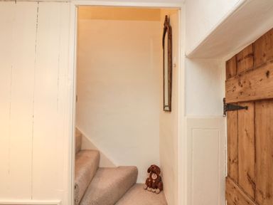 A carpeted staircase with a stuffed dog toy at the bottom next to a wooden door and a wall mirror at 12 Castlegate in Pickering