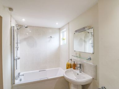 A bathroom with a bathtub shower combination a sink with a mirror and a small window at 12 Castlegate in Pickering