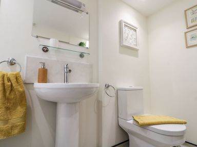 A bathroom with a pedestal sink and toilet with yellow towels and framed pictures on the wall at 12 Castlegate in Pickering