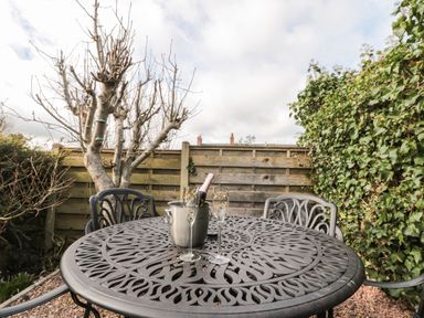 A metal outdoor table with two glasses and a champagne bottle in an ice bucket in a garden with a wooden fence and leafless and leafy plants at 12 Castlegate in Pickering