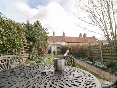 A metal patio table with two glasses and a bottle in an ice bucket in a garden with plants fences and a row of houses at 12 Castlegate Pickering