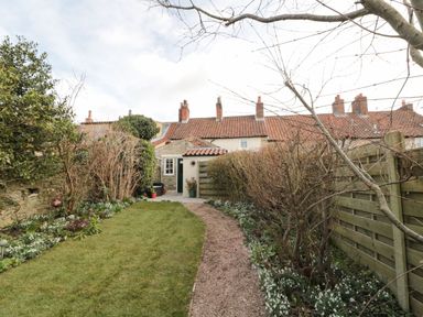 A garden with a grass lawn a gravel path bushes and a house with red roof tiles at 12 Castlegate in Pickering