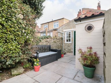 A small outdoor patio with a black bench, potted plants, and stone walls at 12 Castlegate in Pickering