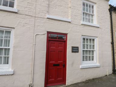 A cream stone cottage exterior with a red door and white framed windows at 12 Castlegate in Pickering