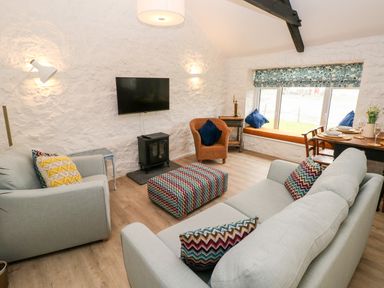 A living room with two light sofas a patterned ottoman a wicker chair and a window seat at Bluebell Cottage Jameston near Manorbier