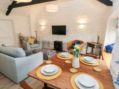 A dining and living area with a wooden table set with plates and glasses and sofas with cushions at Bluebell Cottage in Jameston near Manorbier
