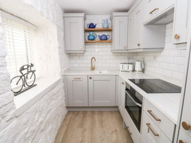 A kitchen with white cabinets and wooden shelves holding blue pottery at Bluebell Cottage Jameston near Manorbier