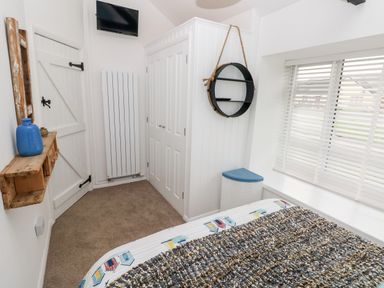 A bedroom corner with a bed a window with blinds a circular wall shelf a wardrobe a wooden wall shelf and a wall-mounted television at Bluebell Cottage in Jameston near Manorbier